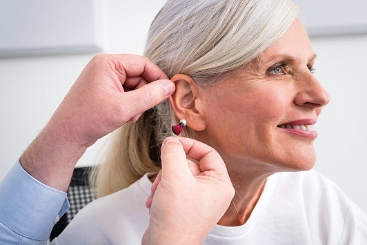 Seniorin bekommt ein modernes Hörgerät vom Hörakustiker ins Ohr eingesetzt.